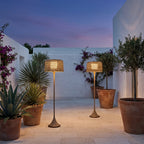 Woven Solar Outdoor Floor Lamp – lit among potted plants at dusk