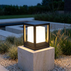 Square Black Solar Fence Post Light – lit on a stone plinth beside a pool
