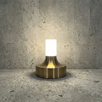 Ebba Table Lamp – lit against a concrete wall, brass finish