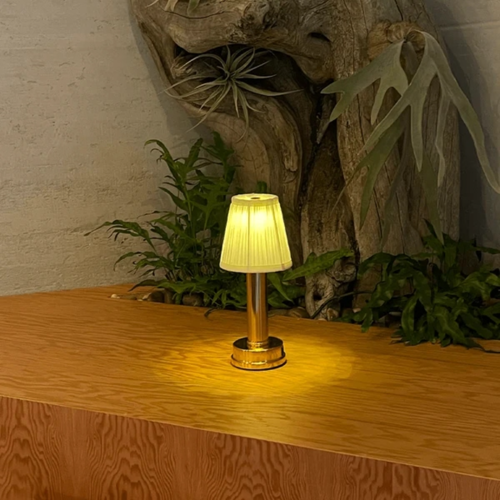 Wren Fabric Table Lamp – lit on a counter beside driftwood and ferns