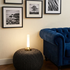 Ebba Table Lamp – on a knitted pouf beside a blue armchair