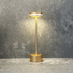 Halden Cordless Table Lamp – lit against a stone wall, gold finish
