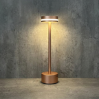Halden Cordless Table Lamp – lit against a stone wall, copper finish