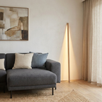 Linden Wooden LED Floor Lamp – lit leaning against a wall beside a sofa
